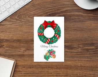 Puede incluir: Una tarjeta de felicitación navideña con una corona de acuarela, un lazo rojo y detalles a rayas. La tarjeta muestra el texto "Merry Christmas" e ilustraciones de regalos envueltos. La tarjeta está sobre una superficie de madera.