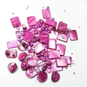 May include: A collection of fuchsia-coloured shell beads in various shapes, including rectangular tiles, irregular rounded pieces, and small spherical pearls. The beads feature a glossy, iridescent finish with natural variations in texture and depth.