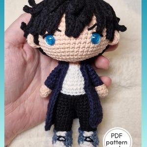 Könnte beinhalten: Handgefertigte Häkelpuppe mit schwarzen Haaren, blauen Augen und einem marineblauen Mantel. Die Puppe trägt ein weißes Hemd, eine schwarze Hose und blaue Turnschuhe. Der Text "PDF pattern only" befindet sich in einem weißen Kreis.