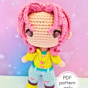 Peut inclure: Poupée au crochet faite à la main, avec des cheveux roses et une veste jaune. La poupée porte un pantalon bleu avec des cœurs roses et des chaussures jaunes. Le texte "PDF pattern only" est inclus.