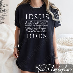 Puede incluir: Camiseta negra con la palabra "JESUS" en blanco, encima de un poema sobre las acciones de Jes&uacute;s, que termina con "DOES". La camiseta tiene un corte relajado y es adecuada para el uso diario.