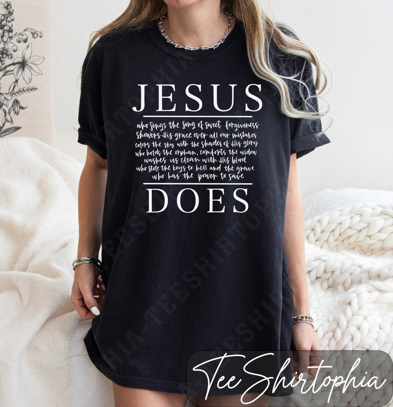 Puede incluir: Camiseta negra con la palabra "JESUS" en blanco, encima de un poema sobre las acciones de Jes&uacute;s, que termina con "DOES". La camiseta tiene un corte relajado y es adecuada para el uso diario.