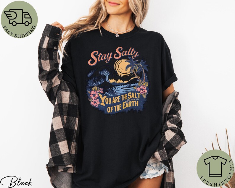 May include: Black t-shirt with a tropical graphic featuring a wave, palm trees, and the text "Stay Salty. You are the salt of the earth." The shirt has short sleeves and a relaxed fit.