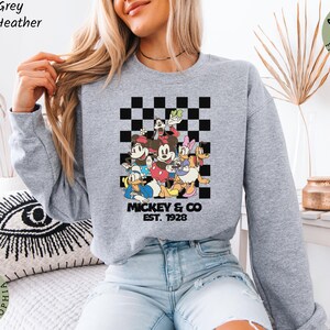 May include: Sport grey athletic heather sweatshirt featuring a colorful graphic of Mickey Mouse and friends. The design includes Mickey, Minnie, Donald Duck, Daisy Duck, Goofy, and Pluto, with the text "Mickey & Co. EST. 1928".