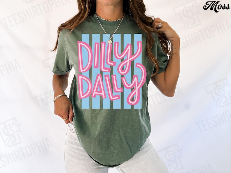 K&ouml;nnte beinhalten: Olivgr&uuml;nes T-Shirt mit dem Schriftzug "Dilly Dally" in rosa Schrift auf hellblau gestreiftem Hintergrund. Das T-Shirt hat einen l&auml;ssigen Stil und ist f&uuml;r den Alltag geeignet.