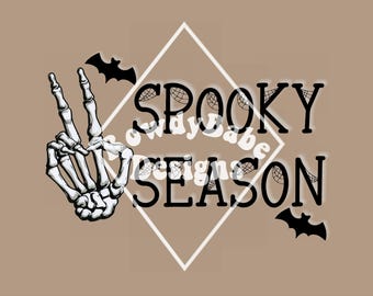 May include: A black and white skeleton hand making a peace sign with the text "Spooky Season" in black letters with a spiderweb design behind the text.