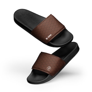 May include: Two black slide sandals with brown straps. The straps feature a repeating wave pattern and the text "BY NERD". The sandals are designed for casual wear and comfort.