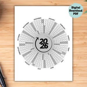May include: A circular 2026 calendar printed on white paper. The calendar is in a radial format with months labeled around the perimeter. The center features the year 2026. The words "Digital Download PDF" are in a teal circle.