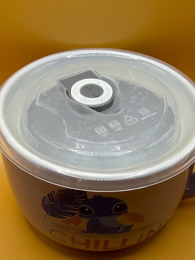 May include: A ceramic bowl with a clear lid. The bowl features a cartoon character illustration and the word "CHILL" in white. The lid has a gray center with a dial and measurement markings. The bowl is white with a purple handle.