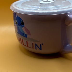 May include: A lavender ceramic bowl with a clear plastic lid. The bowl features a cartoon character illustration and the word "CHILLIN'" in blue. The bowl has a handle and is set against a yellow background.