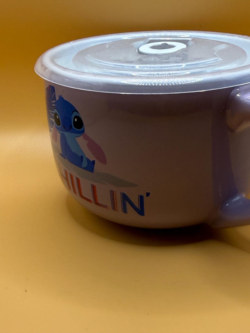 May include: A lavender ceramic bowl with a clear plastic lid. The bowl features a cartoon character illustration and the word "CHILLIN'" in blue. The bowl has a handle and is set against a yellow background.