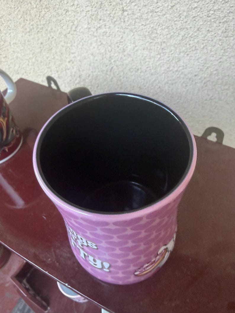 Puede incluir: Una taza de cer&aacute;mica con interior negro y exterior morado claro con un patr&oacute;n de corazones repetidos. La taza muestra texto blanco parcial que dice "gs" y "ry!" junto con un gr&aacute;fico de una porci&oacute;n de pizza en el lateral.
