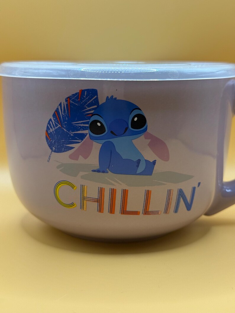 May include: A lavender-colored bowl with a lid featuring a cartoon image of Stitch, with the word "CHILLIN'" in yellow, orange, and blue. The bowl has a handle and is suitable for serving food.