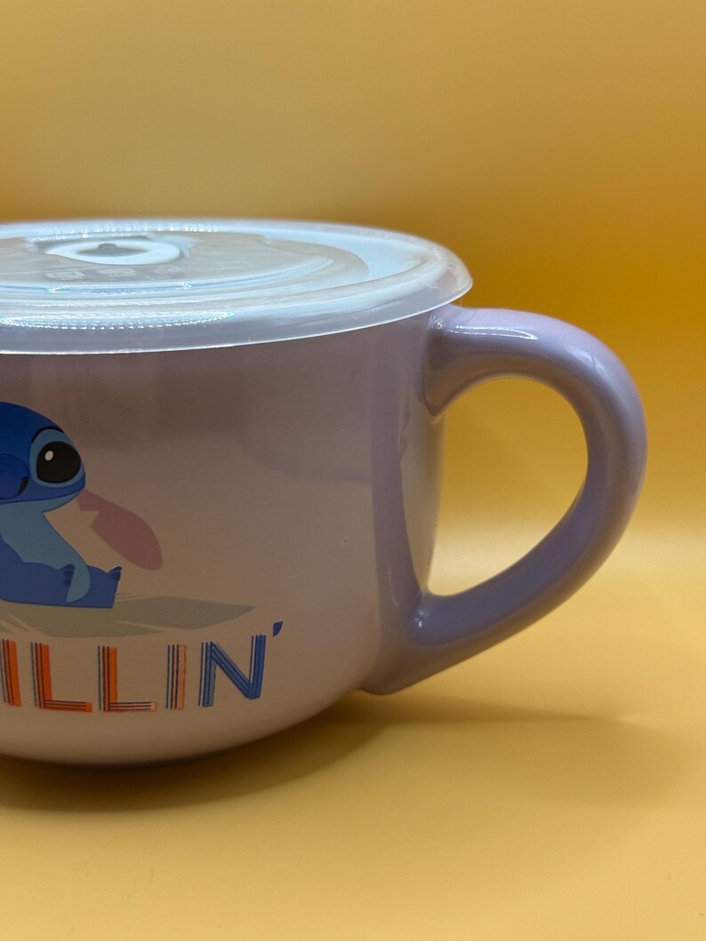 May include: A lavender ceramic mug with a white lid. The mug features a cartoon image of Stitch from Lilo & Stitch, with the word "ILLIN'" in blue and orange. The mug has a curved handle.