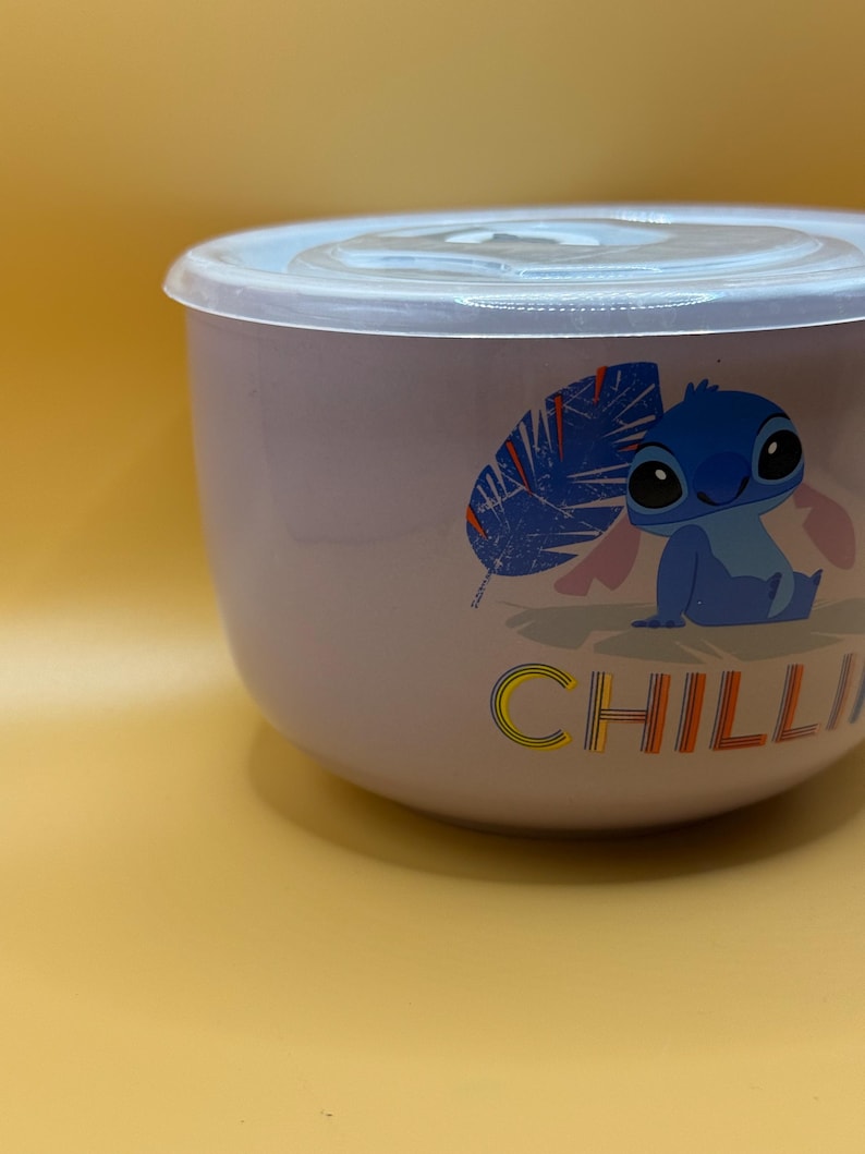 May include: A light purple bowl with a clear lid. The bowl features a cartoon character illustration and the word "CHILLI" in colorful letters. The bowl is likely used for food storage or serving.