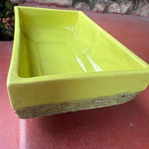 May include: A rectangular, lime green ceramic planter with a textured, brown base. The planter has a glossy finish and is set on a red surface. The planter is empty and ready for use.