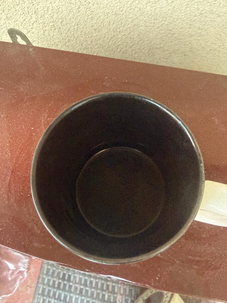 May include: A top-down view of a cylindrical mug featuring a dark brown interior and a white exterior handle. The mug has a smooth, solid-colored finish on the inside and a simple, functional design with a circular opening and a curved handle.