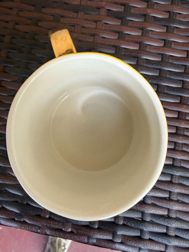 May include: A yellow and cream-colored ceramic mug with a wooden handle. The mug's interior is cream-colored, and the exterior rim is yellow. The handle is made of wood and is attached to the side of the mug.