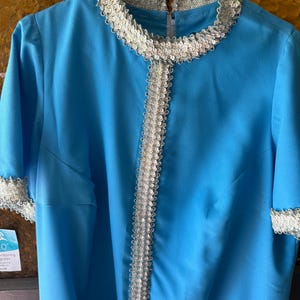 May include: A light blue dress with a white lace trim around the neckline and down the front. The dress has short sleeves and a zipper in the back.