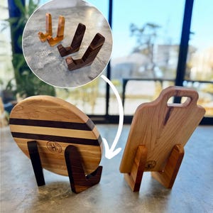 May include: Two wooden cutting boards with a natural wood finish and a compass logo. The boards are displayed on matching wooden stands.