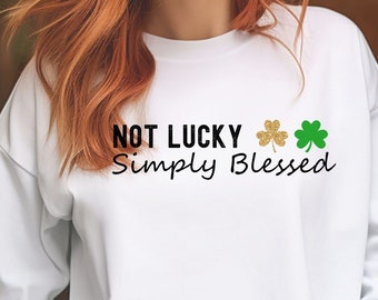 Puede incluir: Sudadera blanca de manga larga con el texto "NOT LUCKY Simply Blessed" y tres tréboles, uno dorado y dos verdes.