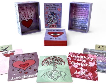 May include: A set of purple and red affirmation cards with illustrations of hearts, a tree, and a guitar. The cards are in a purple box with the text "Love Is Always The Way" on the front. The cards are designed to help you uplift your spirit with love.