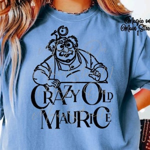 May include: A light blue t-shirt with a black and white illustration of a cartoon character with the text "Crazy Old Maurice" printed on the front.