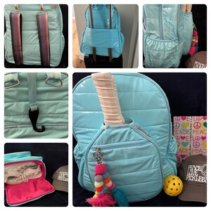 May include: A light blue quilted backpack with a paddle-shaped pocket, a zippered pocket, and a hanging charm. The backpack has a black hook and a white and black paddle inside the pocket. The backpack is sitting on a table with a yellow pickleball, a brown hat with the text "Peace Love Pickleball", and a notebook with the text "Peace Love" repeated.