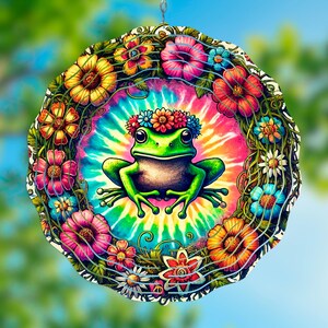 Może przedstawiać: Kolorowy wiatraczek metalowy z zieloną żabą w koronie z kwiatów w środku. Żaba jest otoczona wzorem tie-dye i wieńcem z kwiatów.