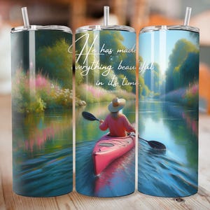 May include: A stainless steel tumbler with a scenic design featuring a person kayaking on a river. The tumbler has a straw and the text "He has made everything beautiful in its time" from Ecclesiastes 3:11. The design includes a pink kayak and lush greenery.