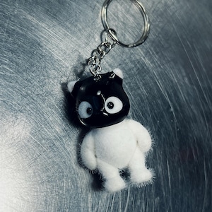 May include: A keychain featuring a small, plush bear with a black head and white body. The bear has large, round eyes and small ears. The keychain includes a silver-colored ring and chain.