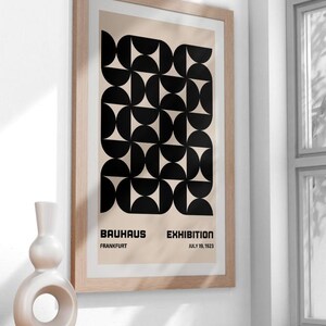 May include: A framed poster with a black and white geometric design. The poster reads "Bauhaus Exhibition, Frankfurt, July 19, 1923".