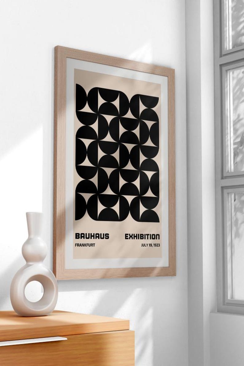 May include: A framed poster with a black and white geometric design. The poster reads "Bauhaus Exhibition, Frankfurt, July 19, 1923".