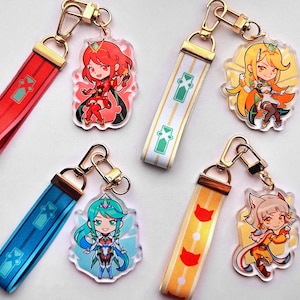 Könnte beinhalten: Vier bunte Anime-Charakter-Schlüsselanhänger mit goldfarbenen Metallringen und Bandbändern. Jeder Schlüsselanhänger zeigt einen anderen Charakter mit einem einzigartigen Design und Farbschema.