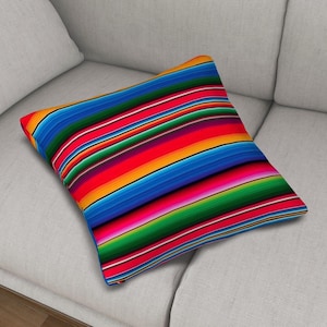 May include: A square throw pillow featuring a vibrant, multi-colored striped pattern. The design consists of horizontal bands in bright shades of red, orange, yellow, green, blue, and purple, creating a bold, repeating sequence across the fabric.