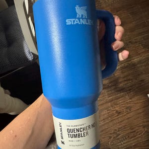 May include: A bright blue Stanley Quencher H2.0 FlowState tumbler with a 1.18 L capacity. The insulated cup features a sturdy side handle, a clear lid, and a white product label printed with the text Stanley The Flowstate Quencher H2.0 Tumbler 1.18 L.