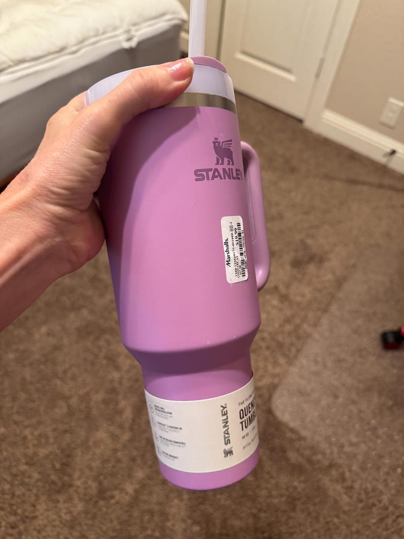 May include: A light purple Stanley Quencher tumbler with a matching handle, a lid, and a white straw. The cup features a metallic rim, a brand logo, and two white product labels attached to the side, one of which includes the text Marshalls.