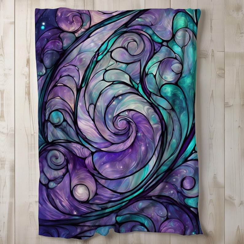 Puede incluir: Una manta decorativa con un dise&ntilde;o de vidriera con patrones arremolinados en tonos morados, turquesas y blancos. El dise&ntilde;o tiene una apariencia de galaxia con un contorno oscuro, creando un aspecto &uacute;nico y art&iacute;stico. La manta se muestra sobre una superficie de madera clara.