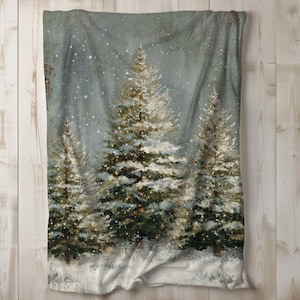 May include: A soft blanket featuring a winter forest scene with snow-covered evergreen trees. The artwork depicts a snowy landscape with falling snowflakes and a muted color palette of greens, whites, and grays. The blanket is draped over a wooden surface.