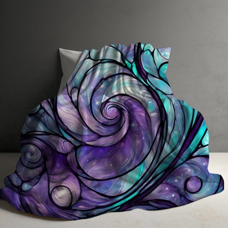 Puede incluir: Una manta suave con un dise&ntilde;o de vidriera arremolinada. El dise&ntilde;o presenta tonos de morado, turquesa y blanco, delineados con l&iacute;neas negras. La manta est&aacute; sobre una almohada blanca.