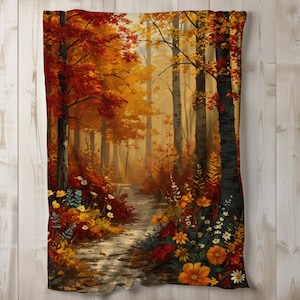 May include: A blanket featuring a vibrant autumn forest scene. The design showcases a path winding through trees with red, orange, and yellow foliage. Wildflowers in shades of yellow, orange, and white line the path, creating a warm and inviting aesthetic.