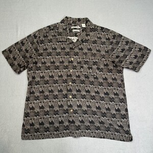 May include: Short-sleeved button-down shirt with a geometric pattern in shades of black, gray, and brown. The shirt has a collared neckline and a chest pocket. The fabric appears to be lightweight.