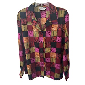 May include: A long-sleeved button-down shirt with a patchwork design. The shirt features a collar and buttoned cuffs. The patchwork pattern includes squares of burgundy, black, pink, orange, and tan with various textures. The label reads "Leslie Haberdahery".