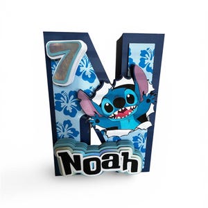 May include: A navy blue letter "N" shaped decoration with a blue floral pattern. The number "7" is on the top left. The character Stitch is bursting through the letter. The name "Noah" is at the bottom.