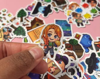 Könnte beinhalten: Ein Aufkleber mit einer Comicfigur einer jungen Frau mit langen roten Haaren, die ein grünes Shirt trägt und eine gelbe Frucht hält. Der Aufkleber ist von anderen Aufklebern mit verschiedenen Designs umgeben, darunter ein Haus, ein Baum und ein Nachthimmel.