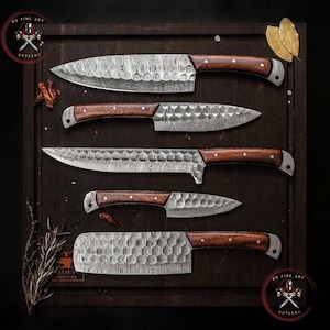 May include: An overhead shot showcases a set of five Damascus steel kitchen knives with wooden handles. The blades have a unique patterned design. The knives are arranged on a dark wooden cutting board, with a logo in the top left and bottom right corners.