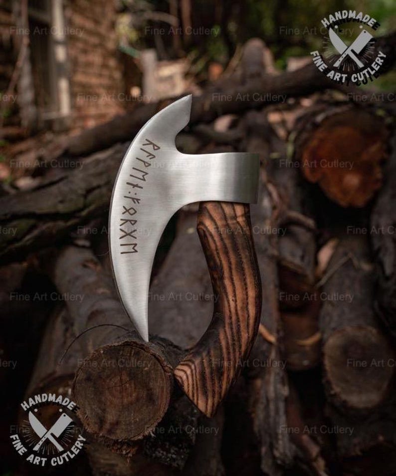 May include: A handmade, curved blade axe with a polished steel head and a dark, wood-grain handle. The blade features etched runes. The axe is displayed against a backdrop of stacked logs, showcasing the craftsmanship.