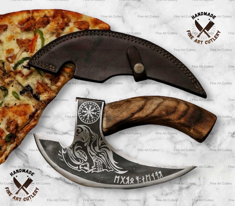 May include: A handmade, curved blade knife with a wooden handle and a leather sheath. The blade features etched designs and text. The knife is displayed with a slice of pizza. The text on the knife reads "MXяя : M1198".