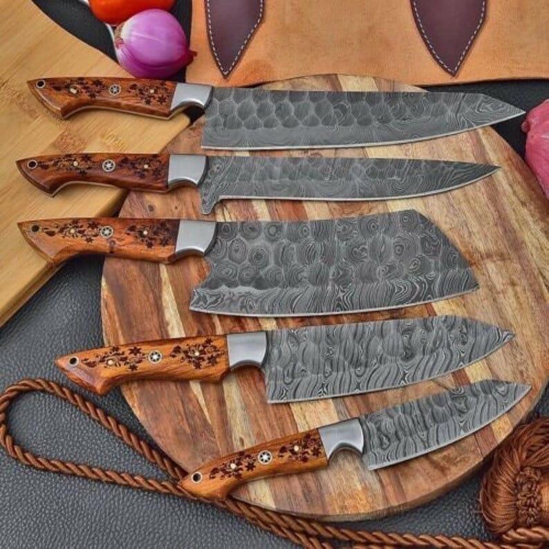 May include: A set of six Damascus steel kitchen knives with wooden handles. The blades have a unique patterned design. The handles are a light brown color with decorative floral accents. The knives are arranged on a wooden cutting board.