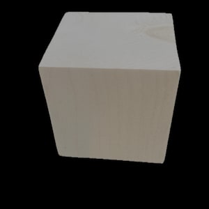 May include: A light-colored, unfinished wooden cube. The cube is a solid block with six flat sides, showcasing the natural grain of the wood. The cube is set against a black background, highlighting its shape and texture.